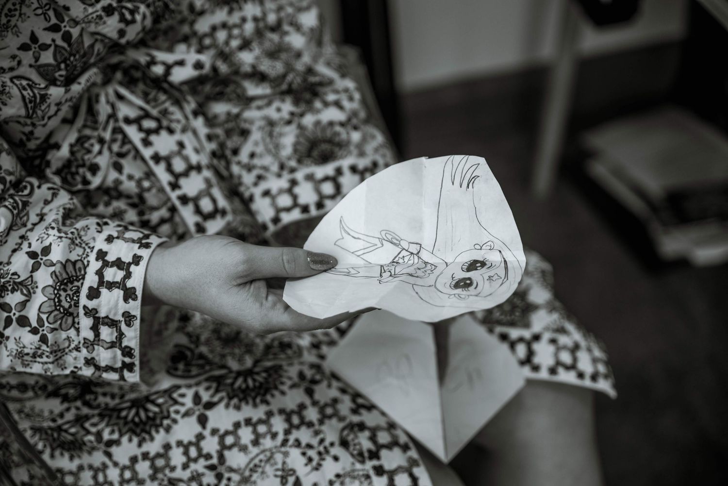 Hands holding a folded paper airplane against a patterned fabric background.