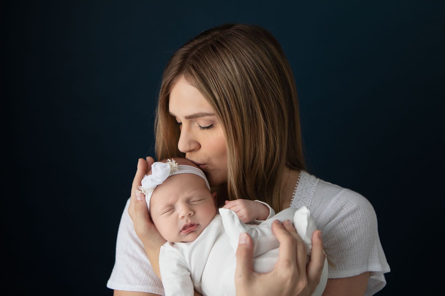 Intimate newborn portrait in dark tones featuring tender maternal moment.