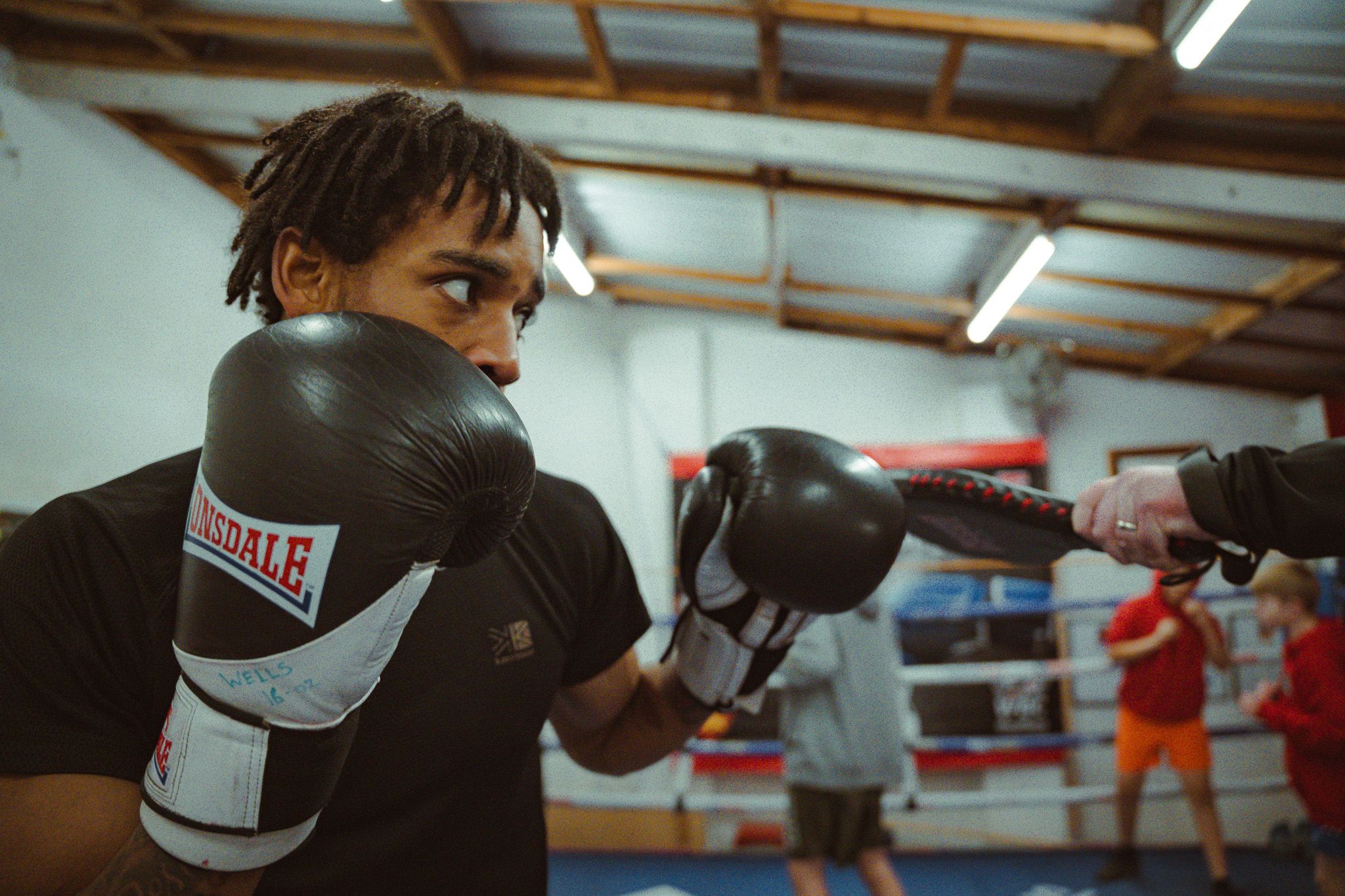 Boxers training in a dimly lit boxing gym with equipment visible in the background.