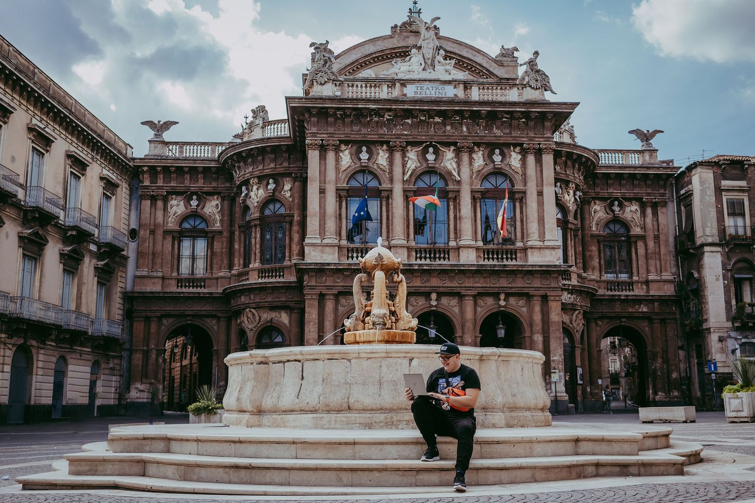 Person sitting on steps in front of the historic Teatro Massimo opera house in Catania, Sicily.