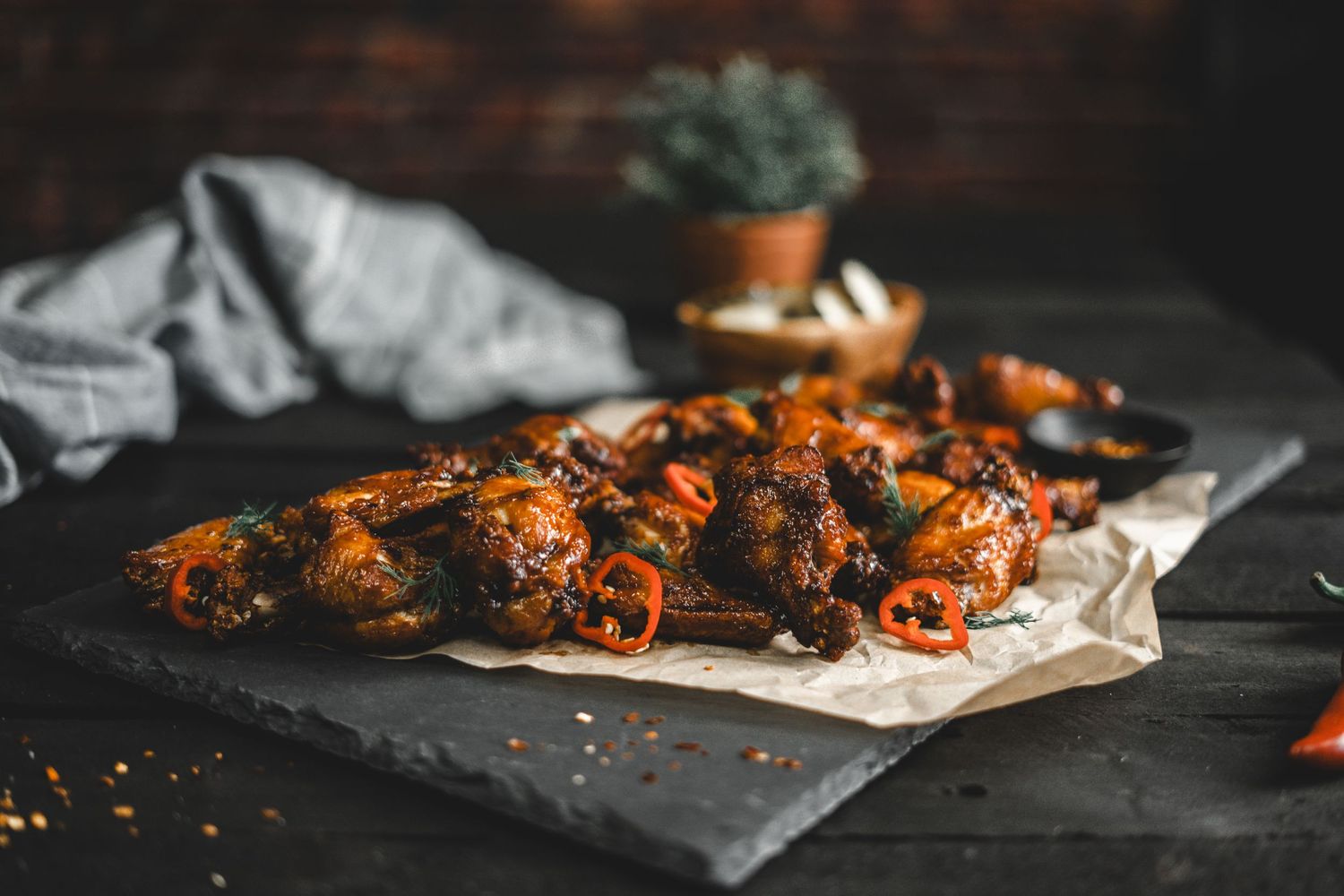 Spicy grilled chicken wings arranged on parchment paper with vibrant red sauce.