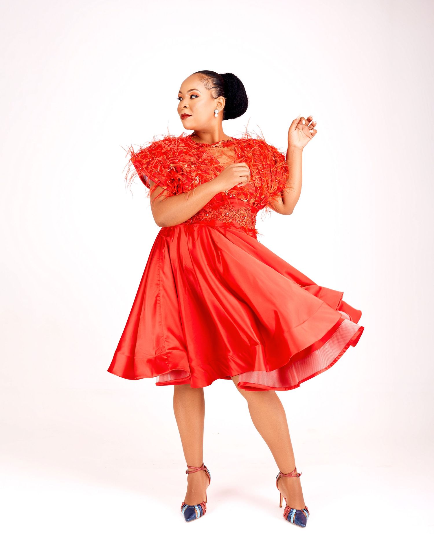 Woman in flowing red dress with feather detail twirls elegantly against white background.