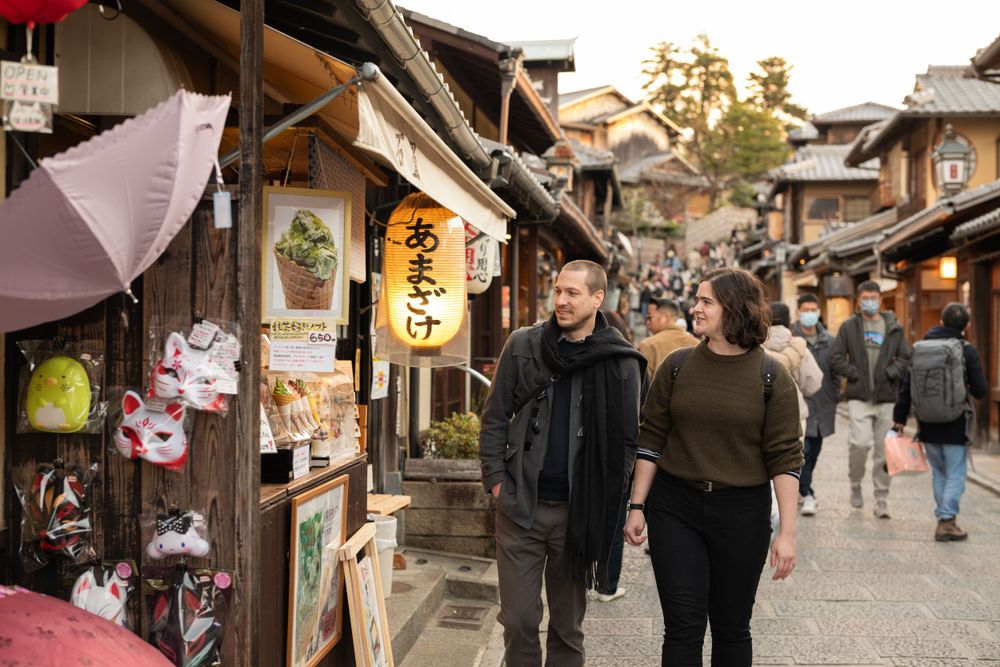 Couple walking past traditional Japanese shops on a bustling street in Kyoto, Japan.