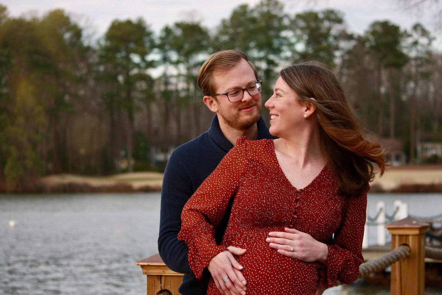 Couple shares intimate moment during lakeside maternity photo session.