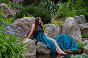 Flowing teal dress contrasts beautifully against natural rock formation and purple flowers in garden in the Hudson Valley,NY.
