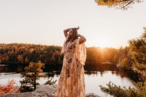 Sunset silhouette on cliff edge with flowing dress against autumn lake landscape.