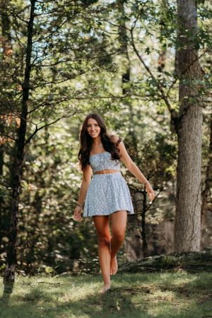 Summer forest photoshoot featuring floral print dress and natural sunlit backdrop.