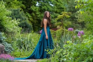 Stunning teal gown sweeps across garden path surrounded by summer flowers and greenery.