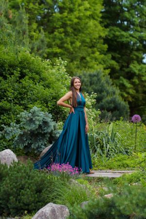 Long teal dress creates dramatic effect in flourishing garden landscape with purple blooms.