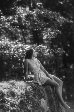 Dreamy black and white portrait of someone in a lace dress reclining on a rock ledge under flowering tree branches.