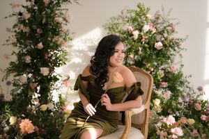 Elegant fashion photoshoot with roses and greenery featuring an olive dress and vintage chair in natural lighting.