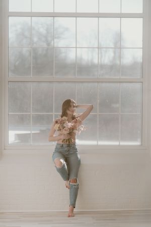 Artistic pose against large windows in distressed denim and floral bouquet in the Hudson Valley,NY.
