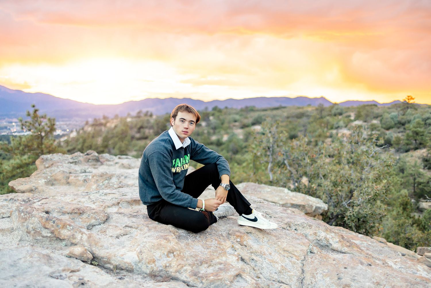 Senior guy sits on the rocks during a fiery sunset at his senior session at Palmer Park in Colorado Springs.