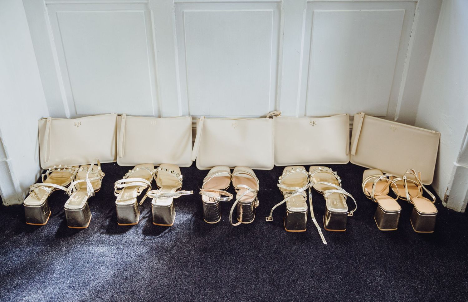 Row of elegant beige wedding shoes arranged neatly on a bench against white paneled walls.
