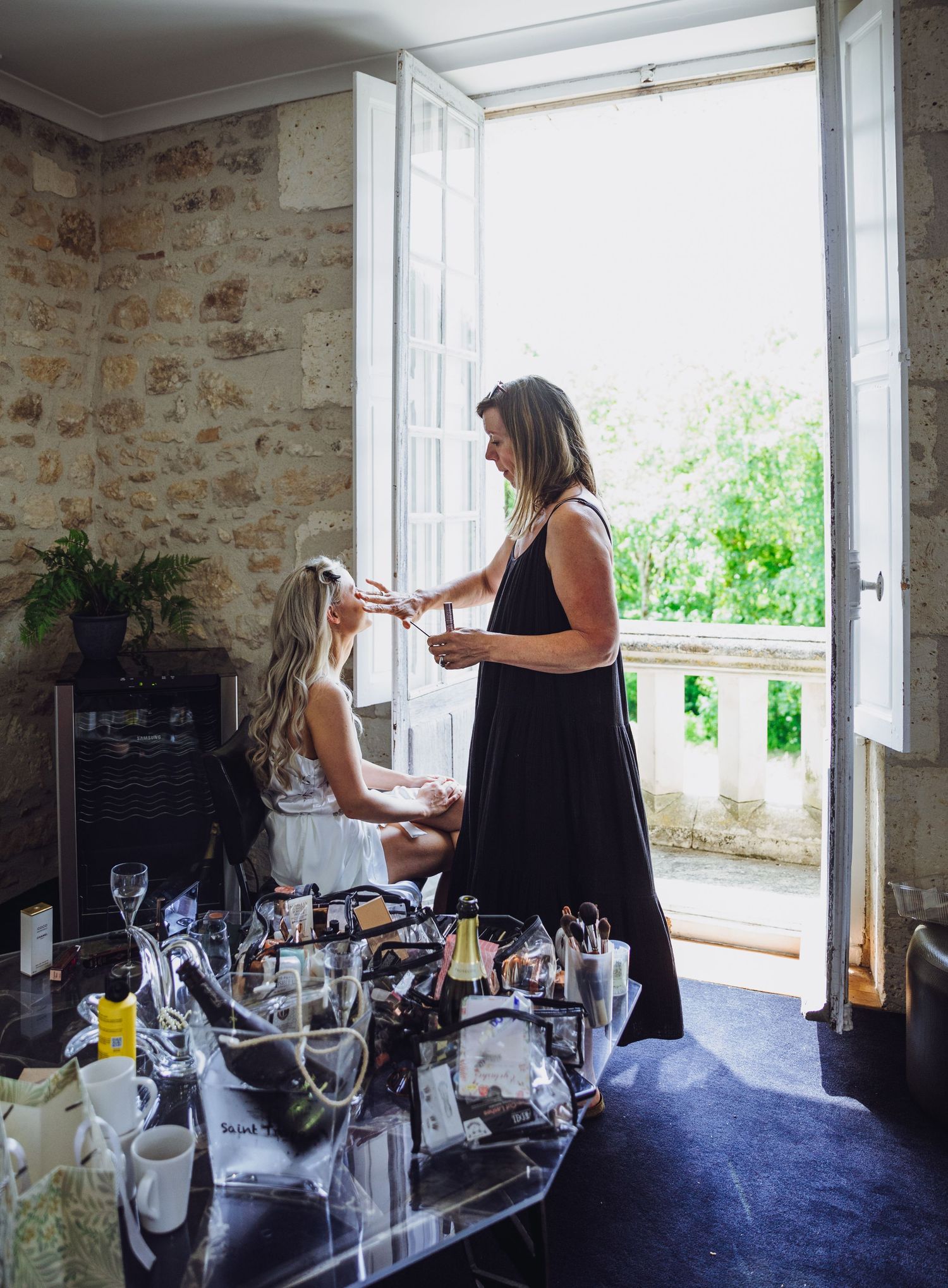 Wedding preparation scene with hair styling taking place by an open window with vintage stone walls.