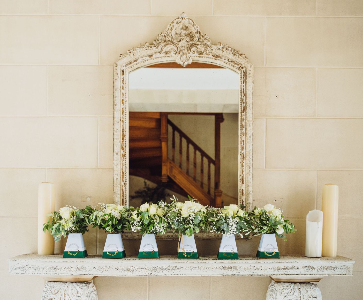 Ornate vintage mirror with white floral arrangements and candles displayed on a mantelpiece.