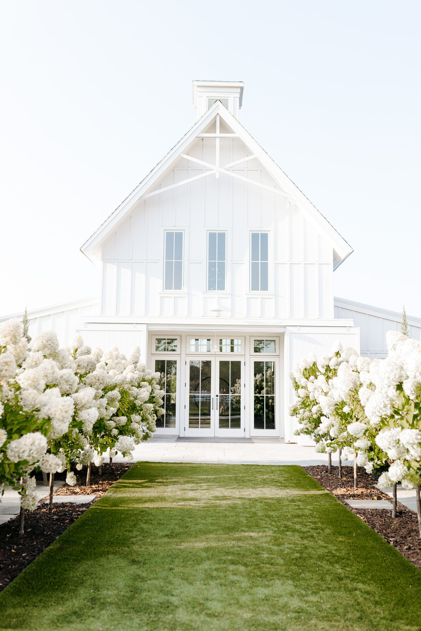 Modern white chapel with French doors and flowering hydrangea bushes lining the entrance path.