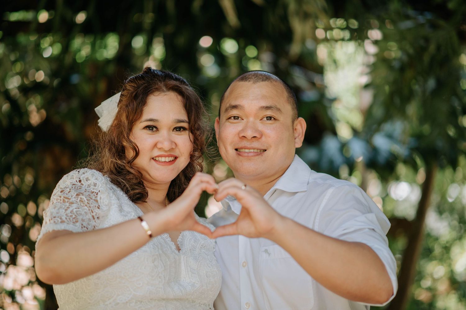 Couple forms heart shape with hands during outdoor wedding photoshoot.