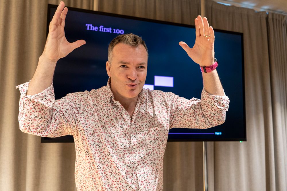 man on stage gesturing with his hands above his head