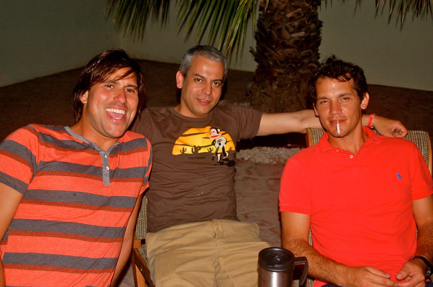 Three friends enjoying a casual evening outdoors under palm trees.