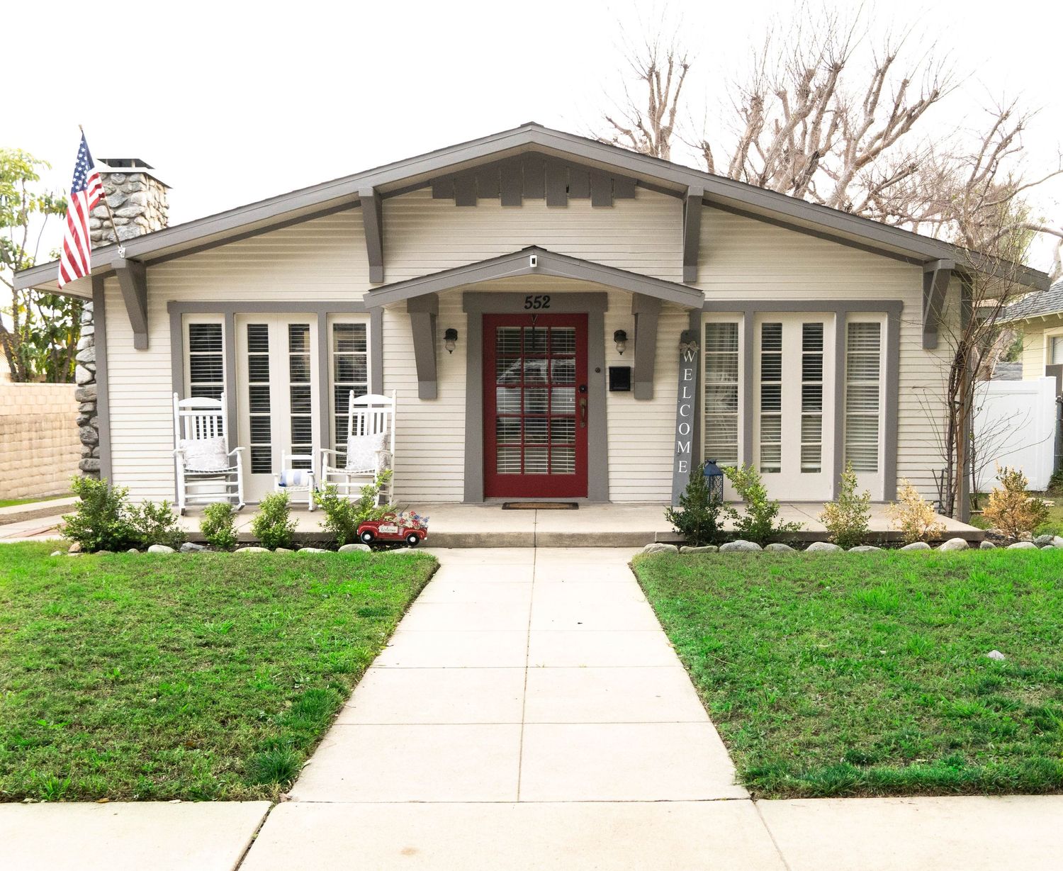 White craftsman style house exterior with red door trim and landscaping.
