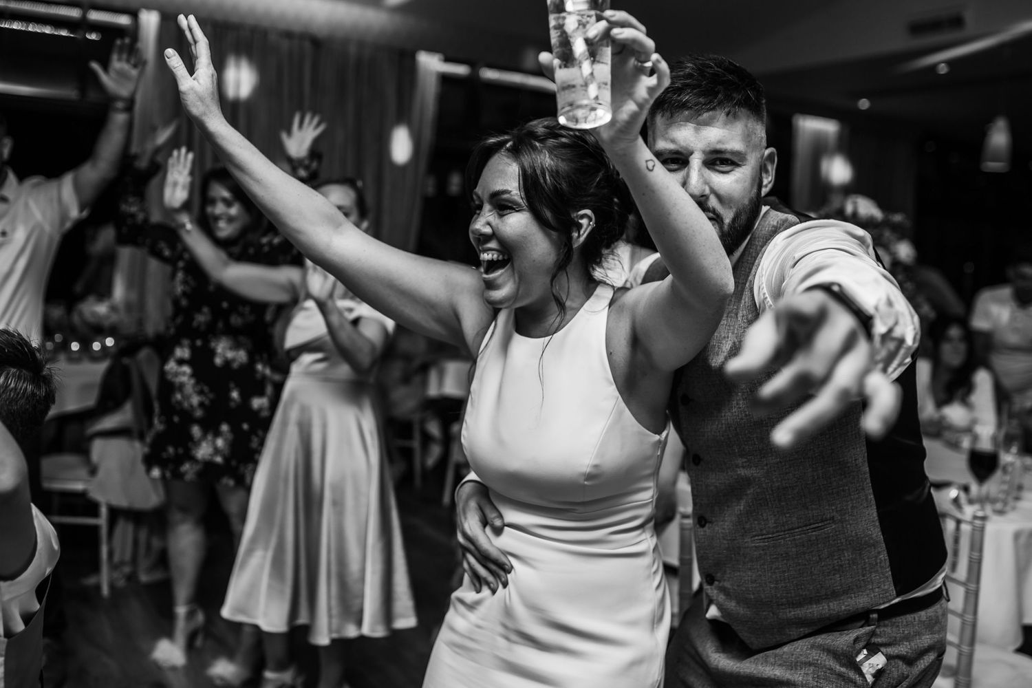 Wedding guests dancing enthusiastically at a reception party in black and white.