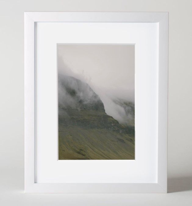 Framed photograph of misty mountains with fog rolling over green slopes.