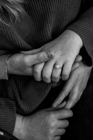 Black and white photo of intertwined hands with an engagement ring.