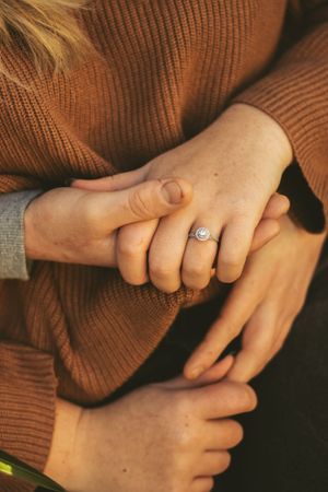 Close-up of hands holding with an engagement ring visible on the feminine hand.