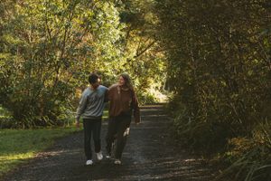 A couple walks together on a tree-lined path in golden afternoon light.