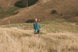 A couple stands together in tall golden grass on a hillside.