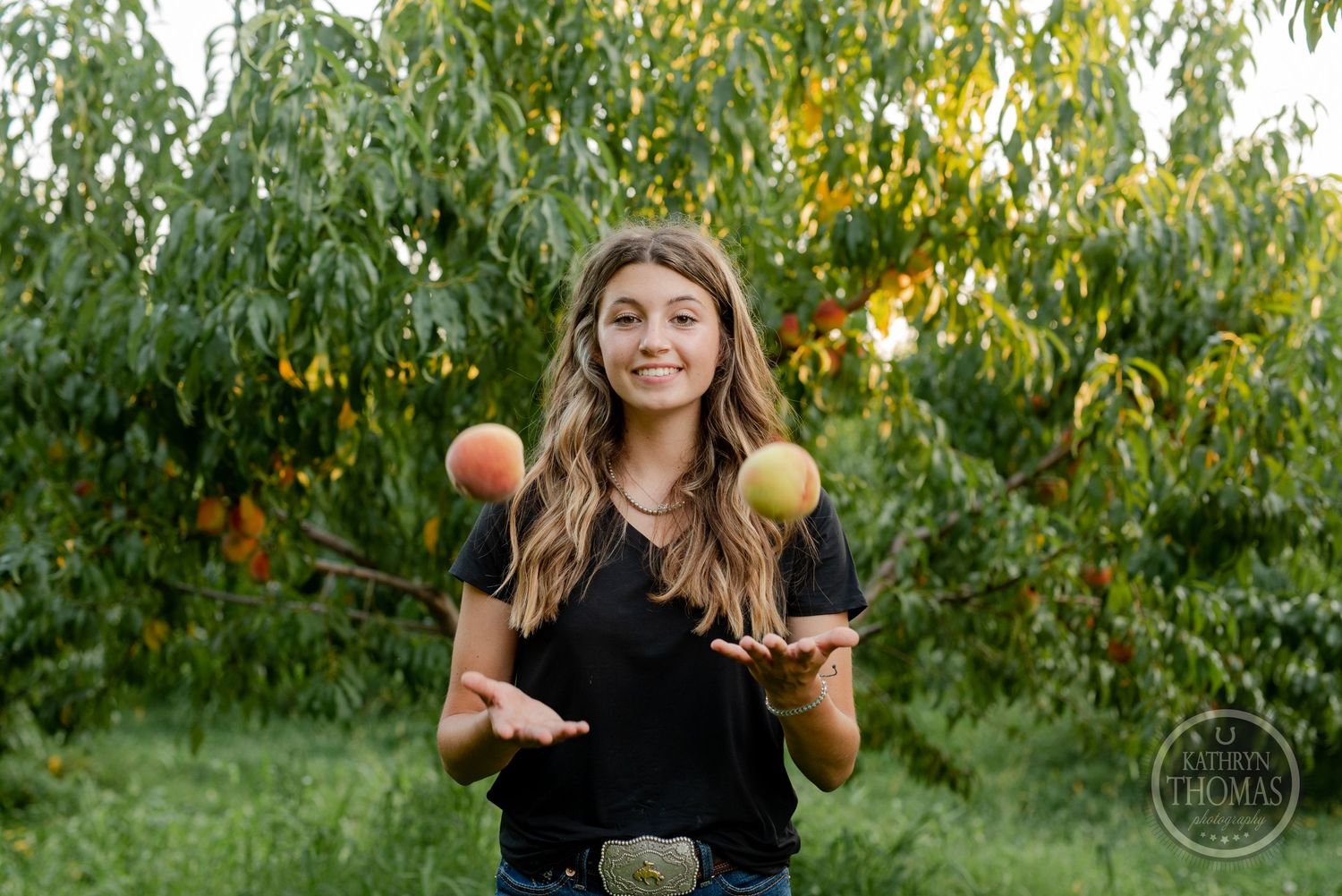 Someone playfully juggling peaches in an orchard during a sunny afternoon photoshoot.
