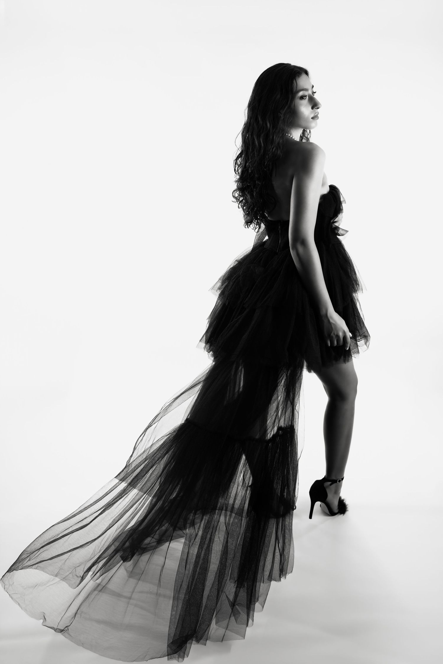 Dramatic fashion poses with black sheer dress flowing against minimalist white backdrop.