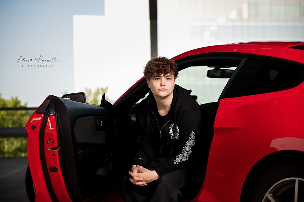 Person in black jacket sitting in doorway of red sports car.