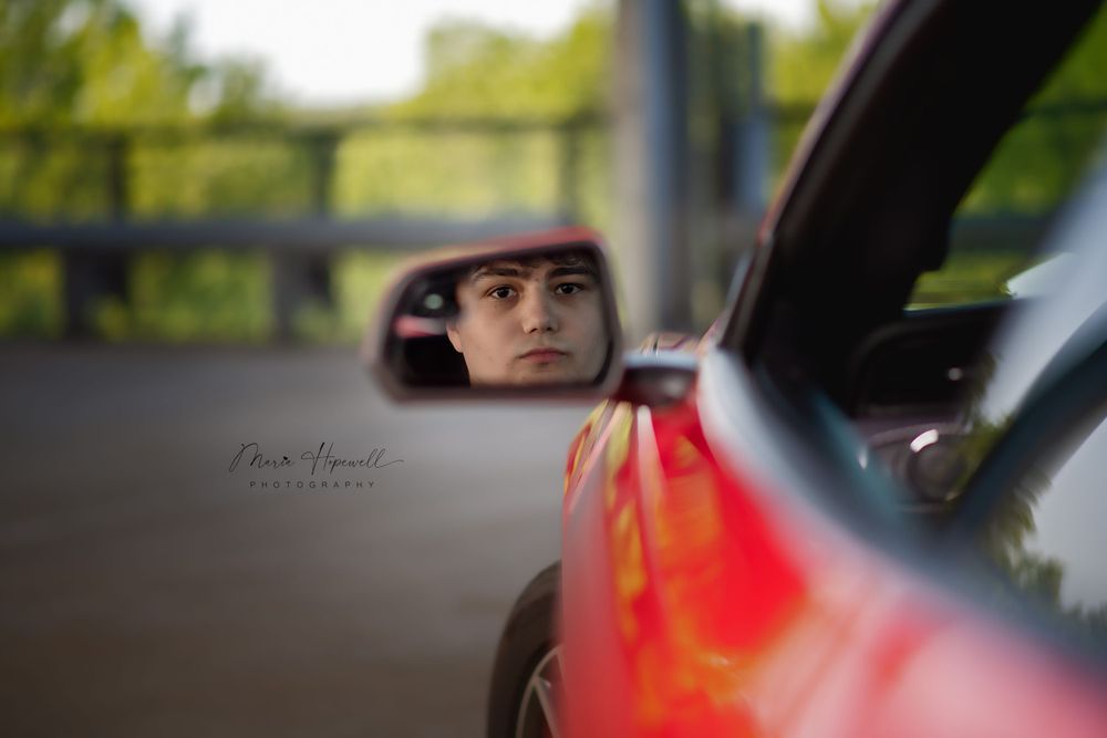 Red car side mirror reflection captured in moody lighting conditions.