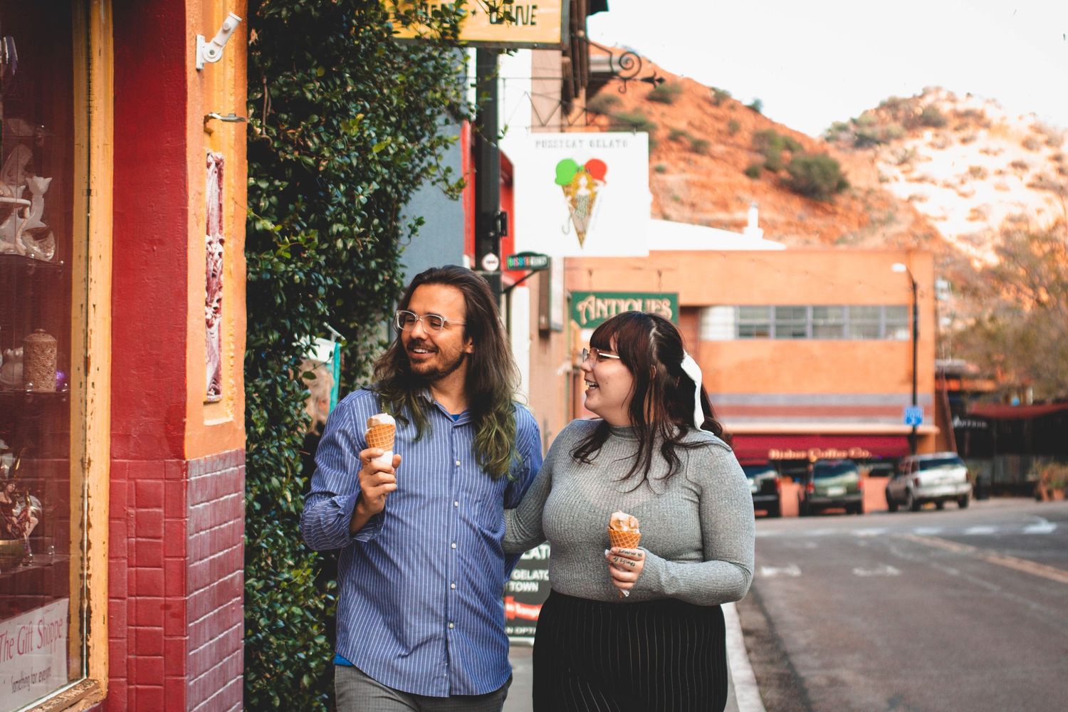 Couple enjoys ice cream cones while strolling past colorful desert town storefronts.
