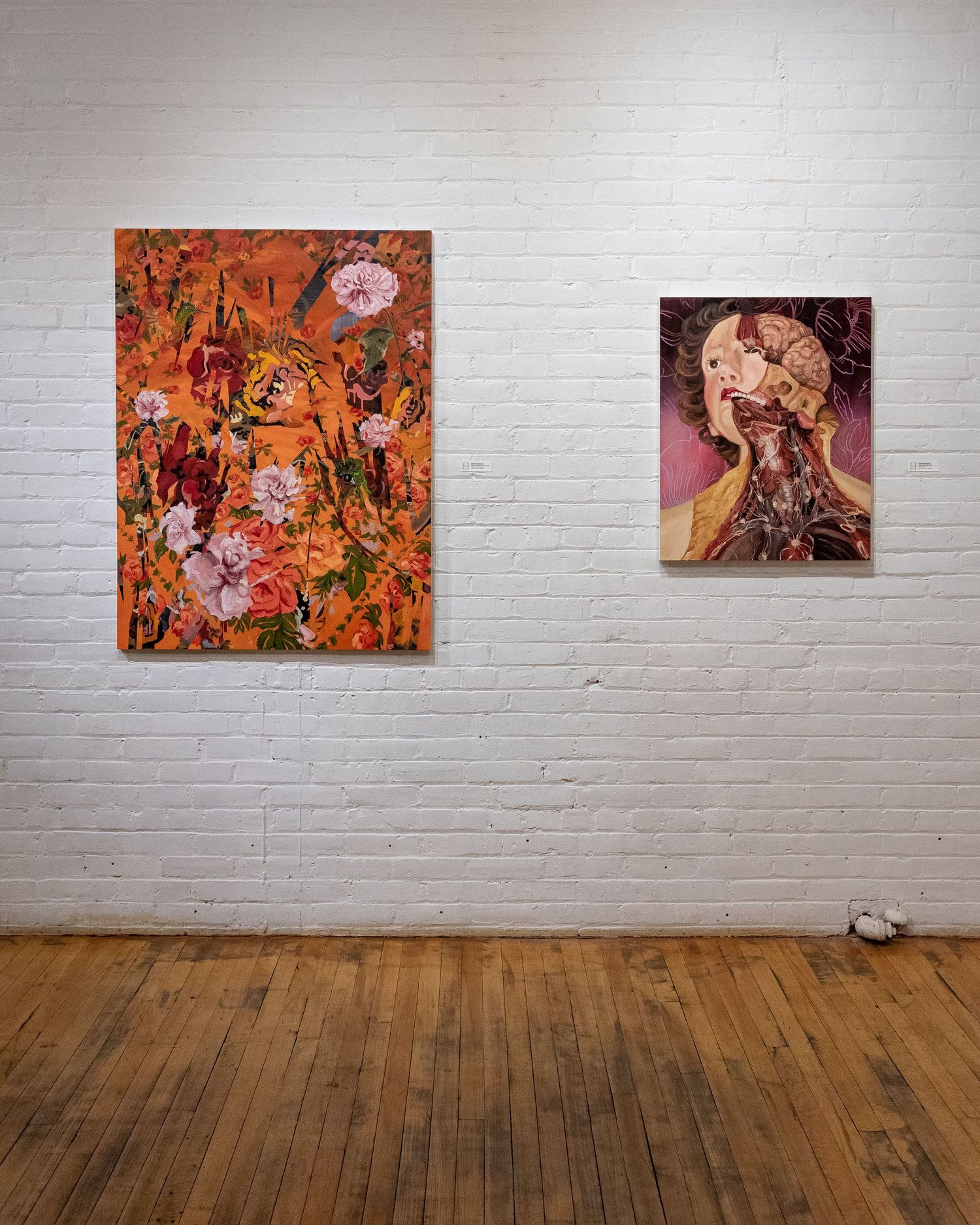 Gallery wall displaying series of orange and pink floral paintings on white brick background.