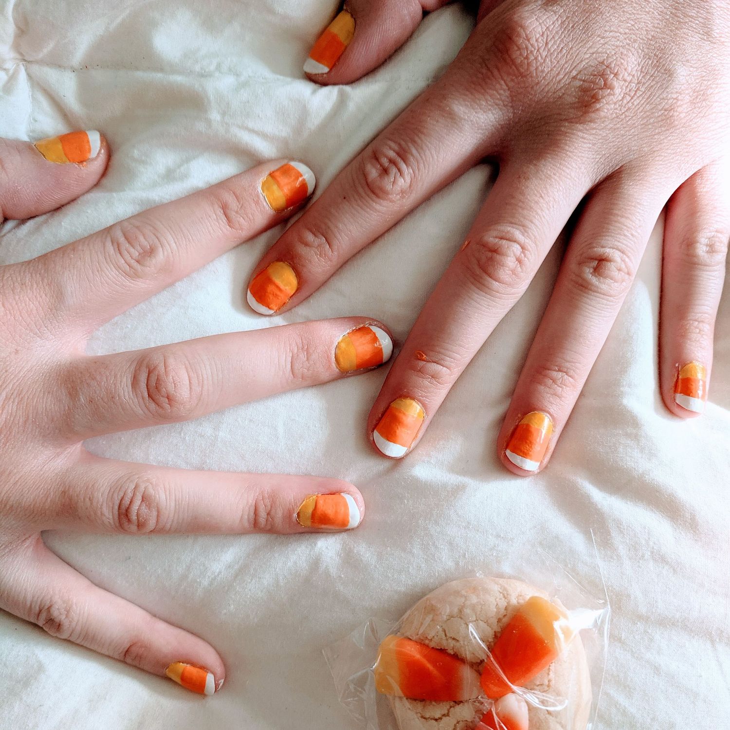 Painted candy corn finger nails spread out on a white blanket