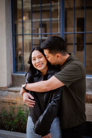 A couple shares an intimate embrace against a blue window backdrop.