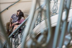A romantic couple photographed through decorative metal railings on stone steps.