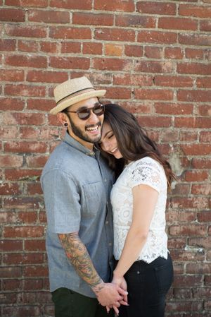 A couple shares a playful moment against a rustic brick wall background.