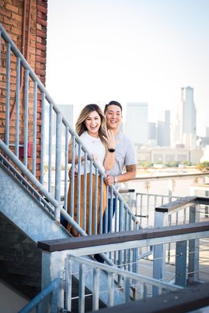 Couple laughing together on brick building staircase with city skyline view.