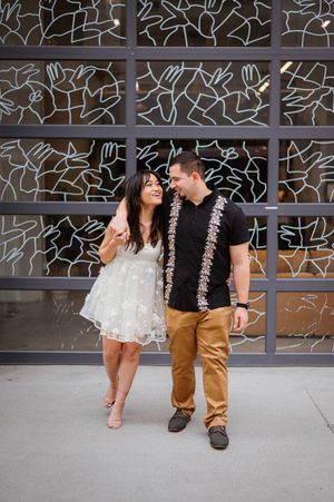 A couple laughs together in front of a geometric patterned wall.
