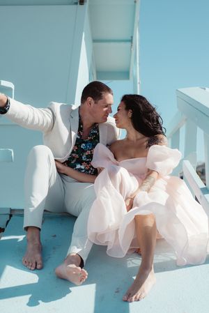 Romantic couple lounges on a turquoise balcony in wedding attire with bare feet.
