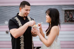 A couple shares ice cream together against a pink wall backdrop.