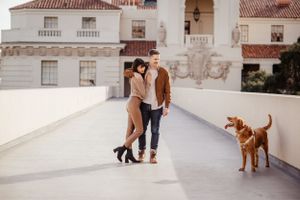 A couple poses with their dog on a white terrace with Spanish colonial architecture.