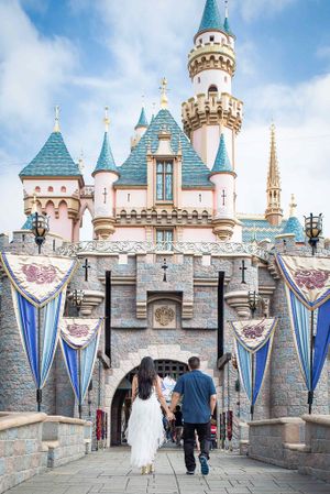 Couple walking through Disneyland castle courtyard with blue banners and turrets.