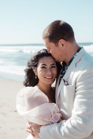 Romantic beach photoshoot with couple in white formal attire.