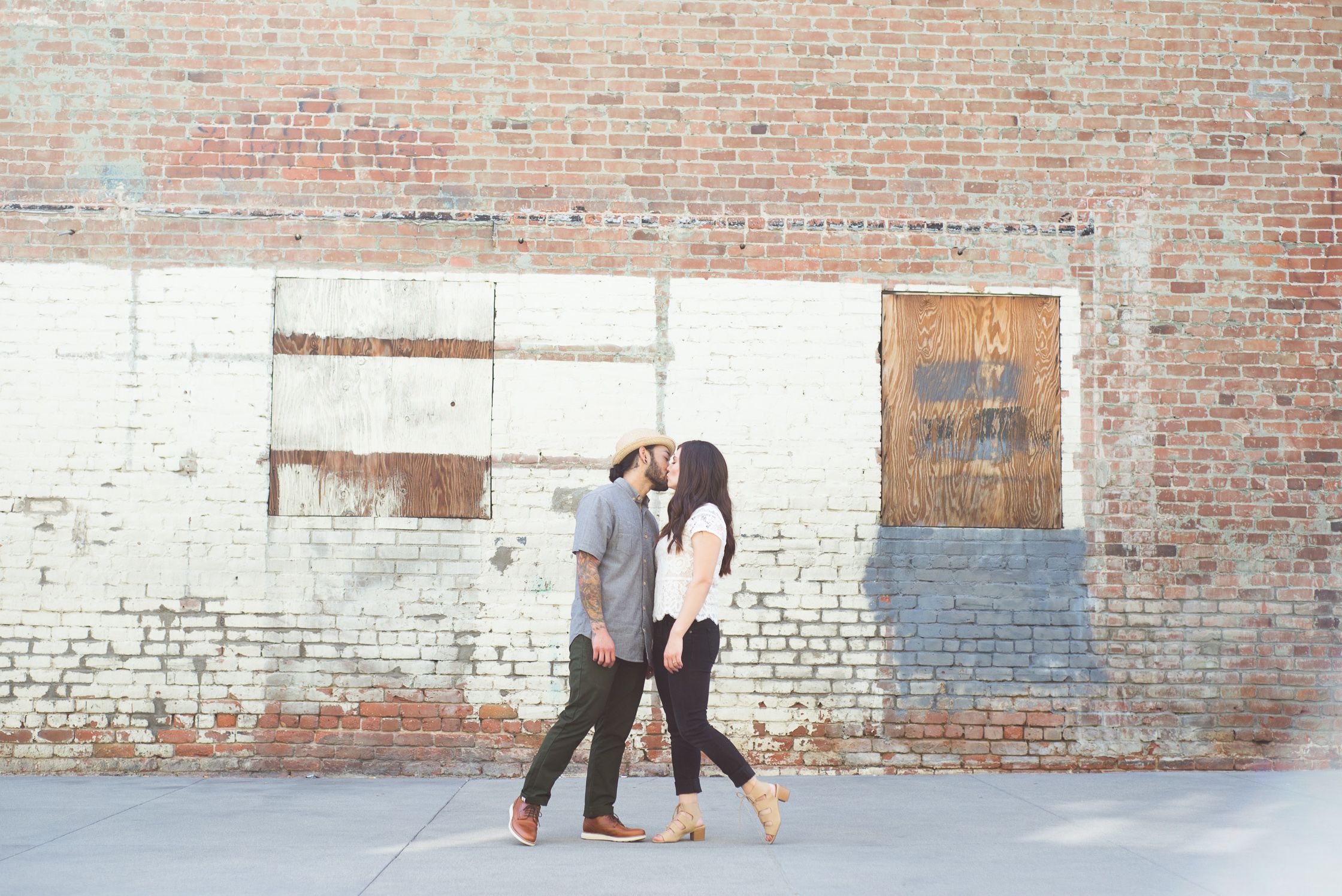 Two people pose playfully against an industrial brick wall backdrop.
