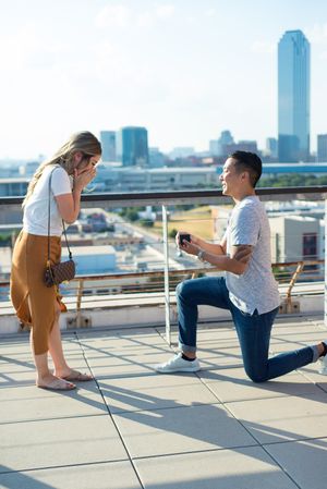 Surprise rooftop proposal moment with city skyline backdrop.